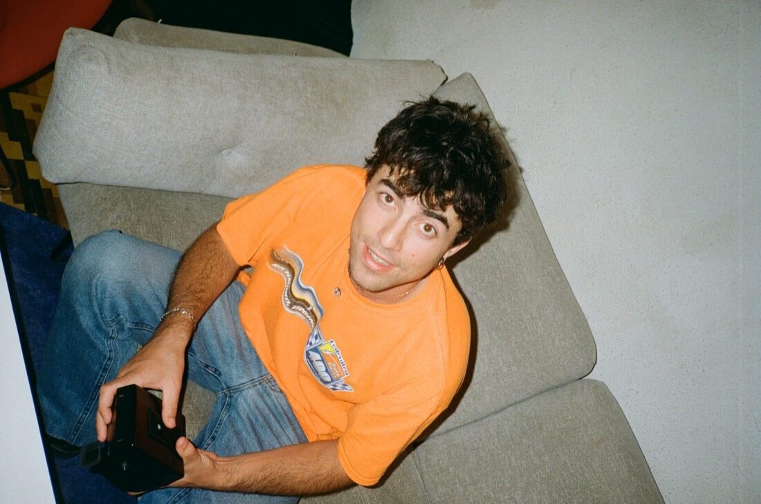 Jojo on a couch holding a camera, looking up at the lens